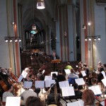 04 - Mēģinājums. Kori aiz mums, priekšā orķestris, diriģents Klauss Eduards Heckers, tālumā - jauniešu koris.